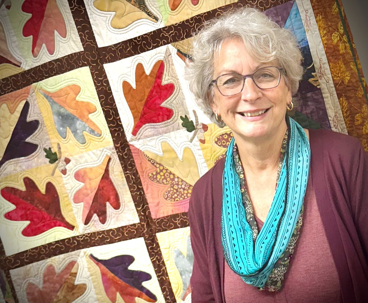 Julie, founder of Sewfunn Dandelion Lessons, in front of one of her quilts